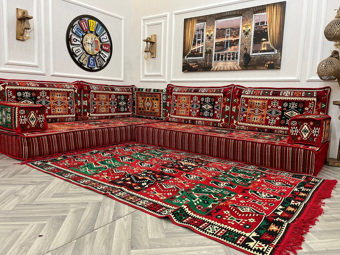 L-shaped Arabic Majlis sofa set with red ethnic floor cushions and a vibrant rug, perfect for cozy living room seating.